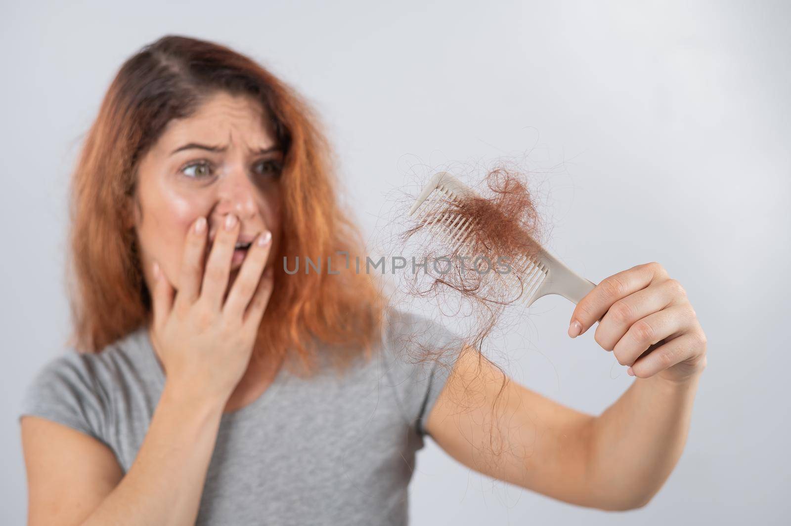 Caucasian woman with a grimace of horror holds a comb with a bun of hair. Hair loss and female alopecia