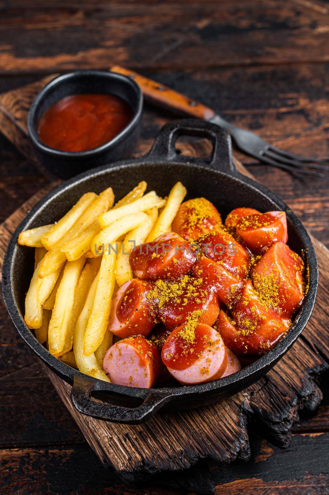 Currywurst street food meal, Curry spice on wursts served French fries in a pan. Dark wooden background. Top view.