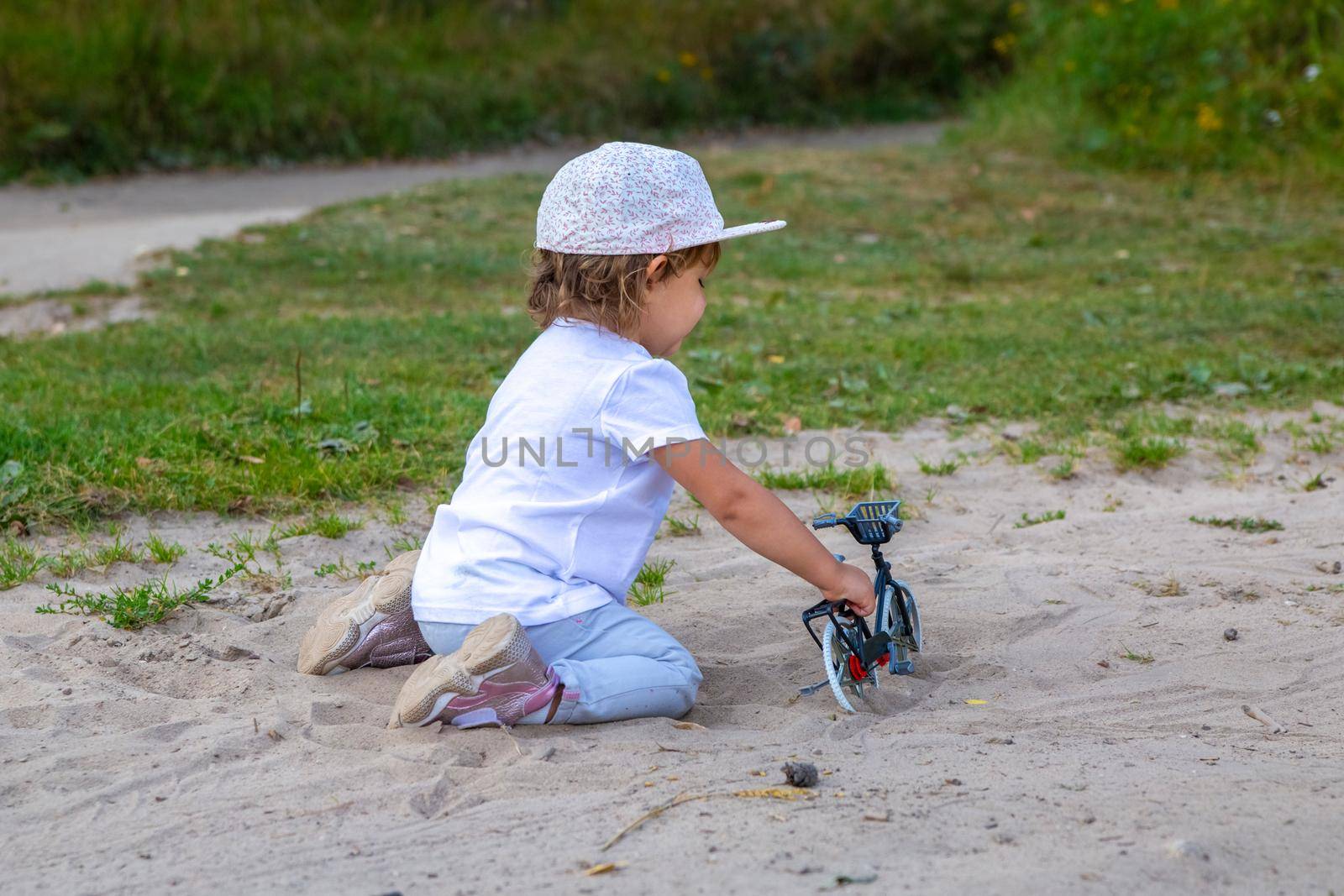adorable toddler plays with a toy bike in nature. child on all fours in the sand on the lawn.