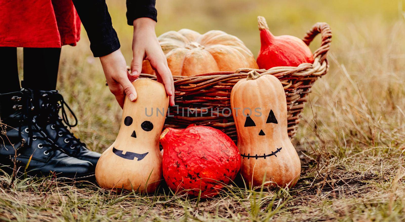 Halloween pumpkins and basket standing at girls feet on autumn ground
