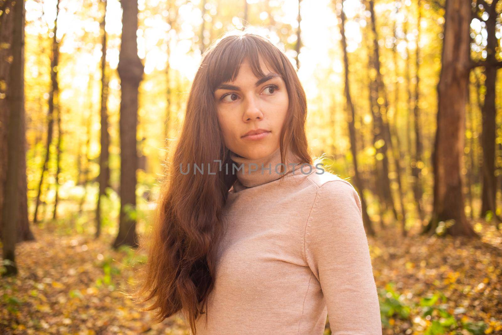 portrait of young beautiful woman in autumn park in sun shines. thinkfull young woman looking away