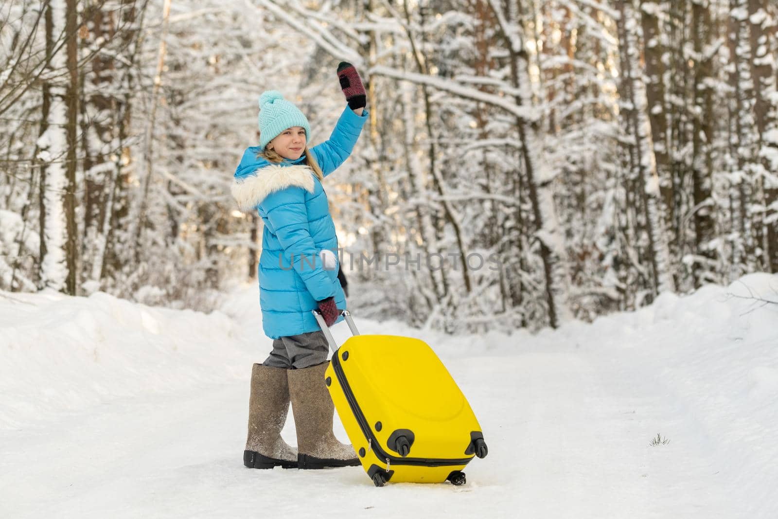 A girl in winter in felt boots goes with a suitcase on a frosty snowy day.