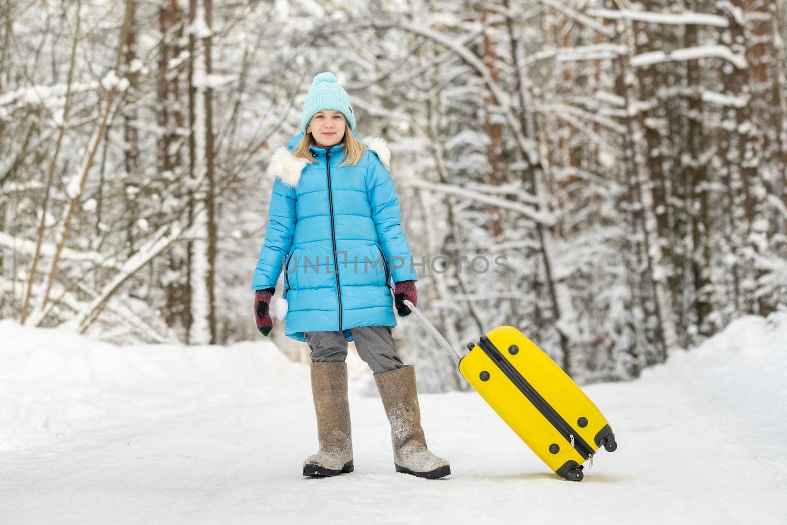 A girl in winter in felt boots goes with a suitcase on a frosty snowy day.