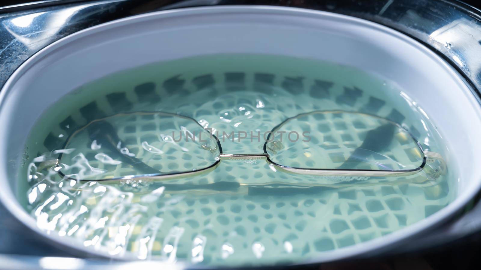 Ultrasound cleaning of glasses in solution. Optical technician repairs the frame of glasses.