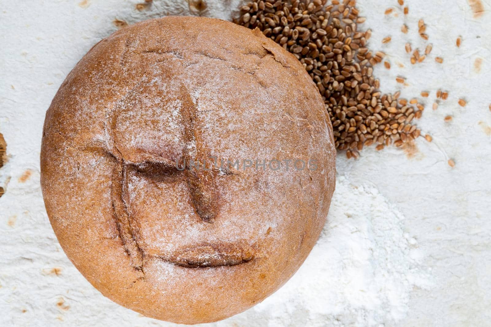 a loaf of freshly baked rye bread, lying on a thin wheat pita bread. Together with bread lies grain and flour. photo close-up, top view