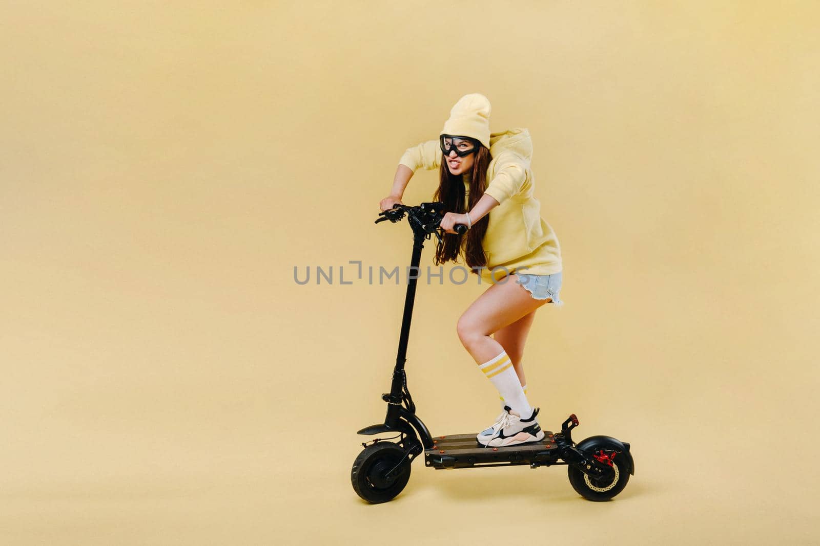 A pregnant girl in yellow clothes on an electric scooter on an isolated yellow background.