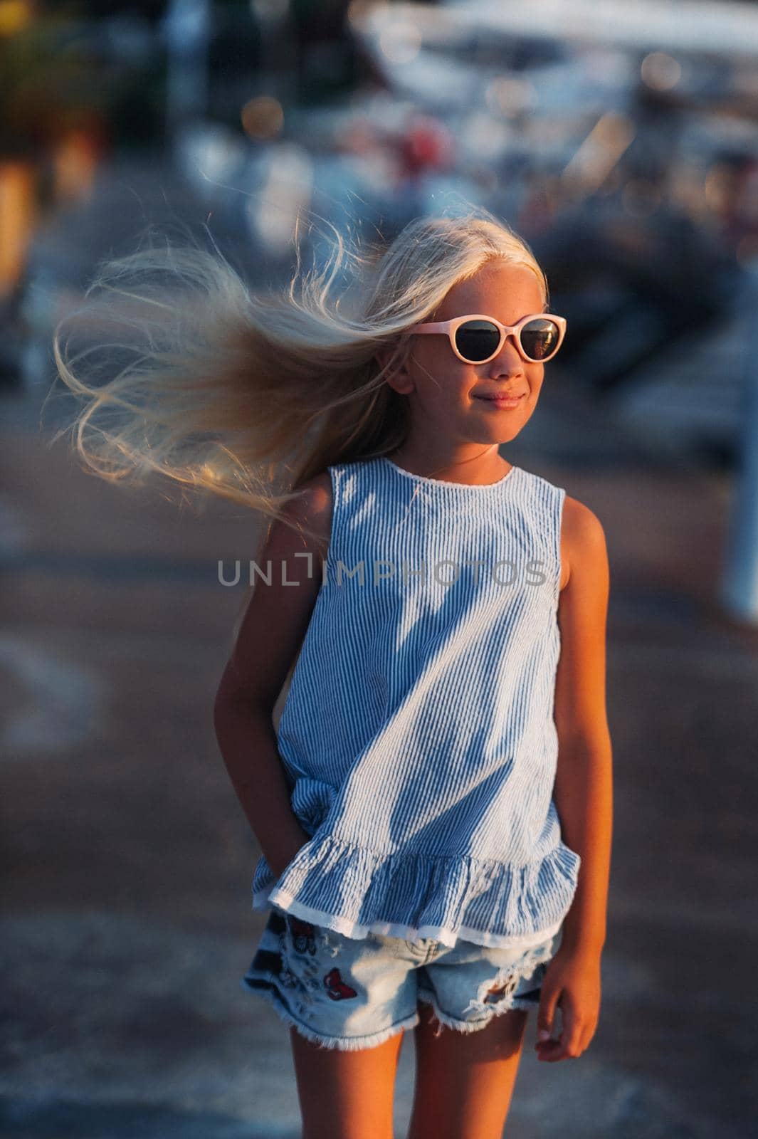 Portrait of a cute smiling ten-year-old girl with glasses.A girl in shorts and a blue t-shirt at sunset near the sea.Turkey.