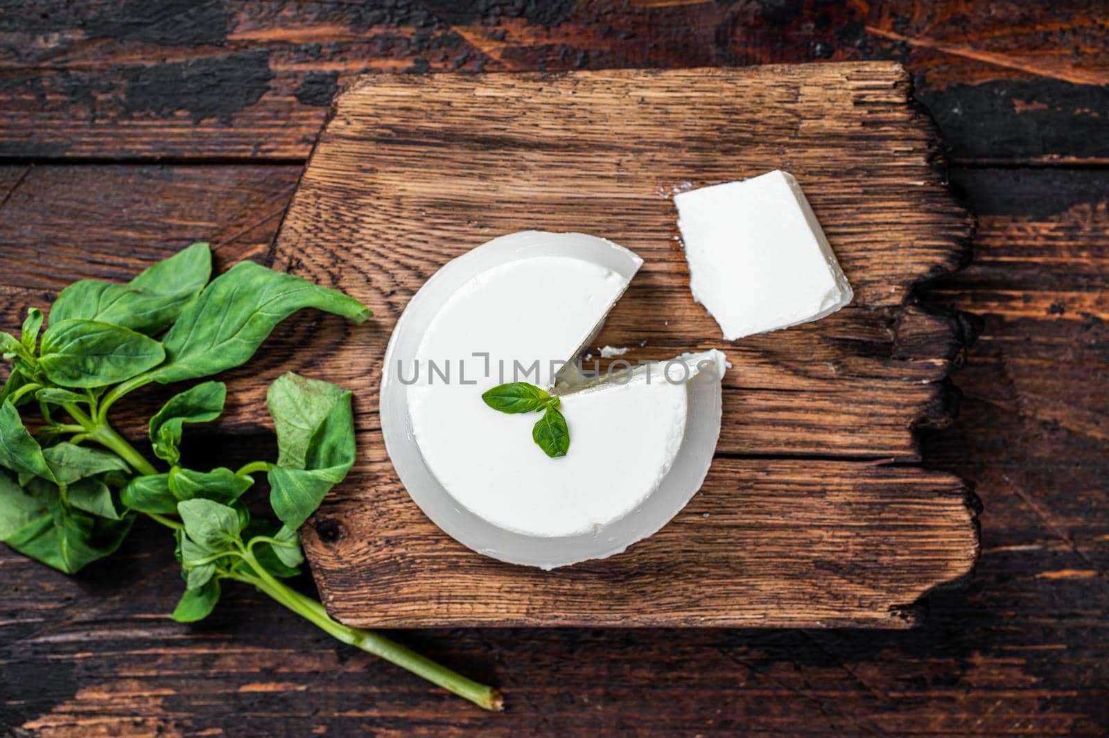 Fresh Ricotta cream Cheese on wooden board with basil. Dark wooden background. Top view by Composter