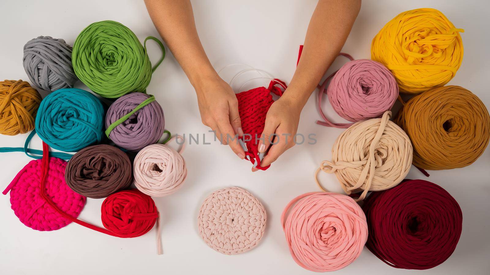 Top view of female hands with knitting on a white table. A woman knits a basket of red cotton yarn