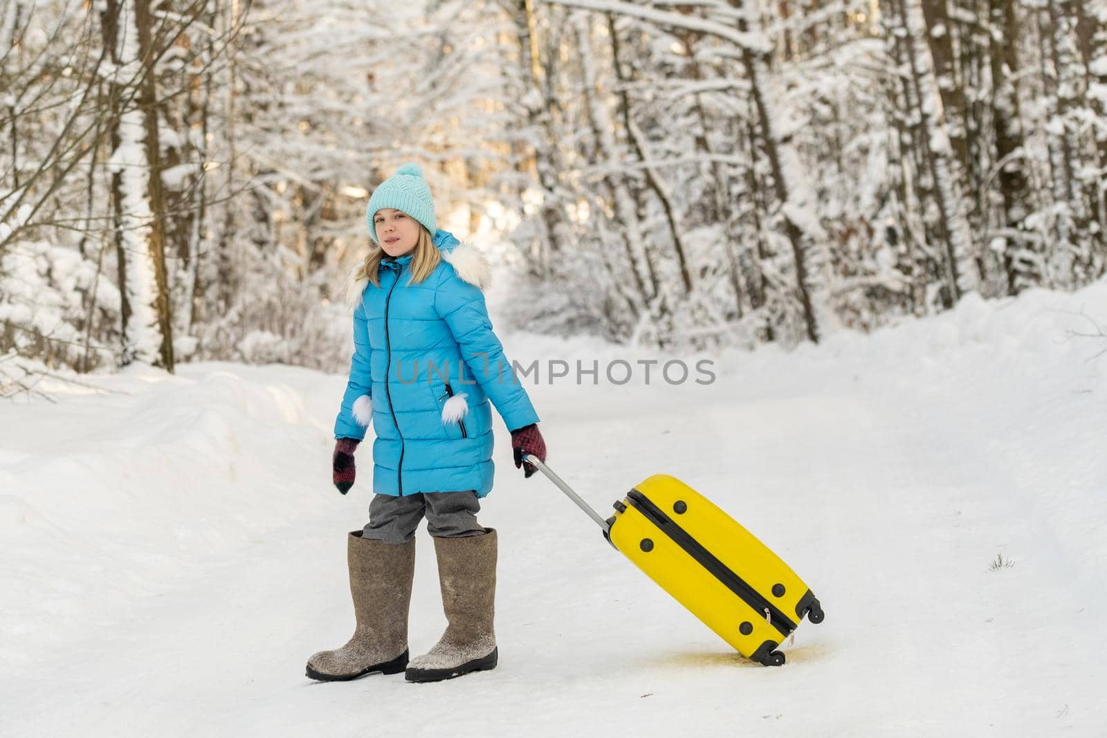 A girl in winter in felt boots goes with a suitcase on a frosty snowy day.