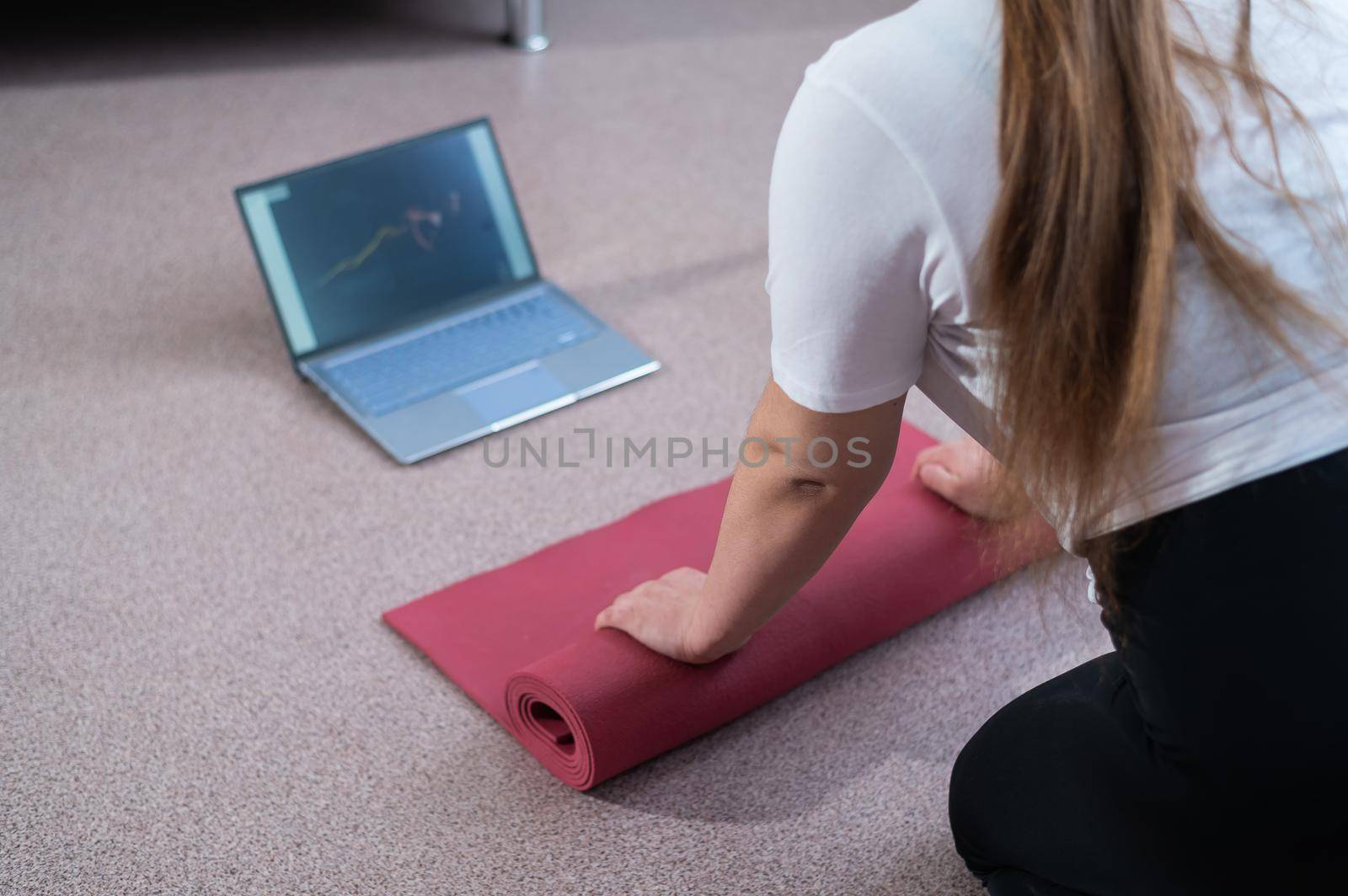 Young chubby woman folds sports mat after online fitness class by mrwed54