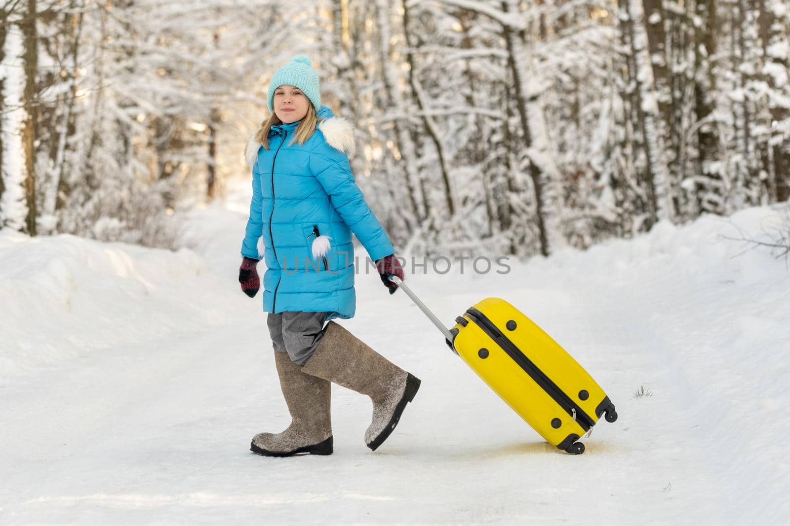 A girl in winter in felt boots goes with a suitcase on a frosty snowy day.