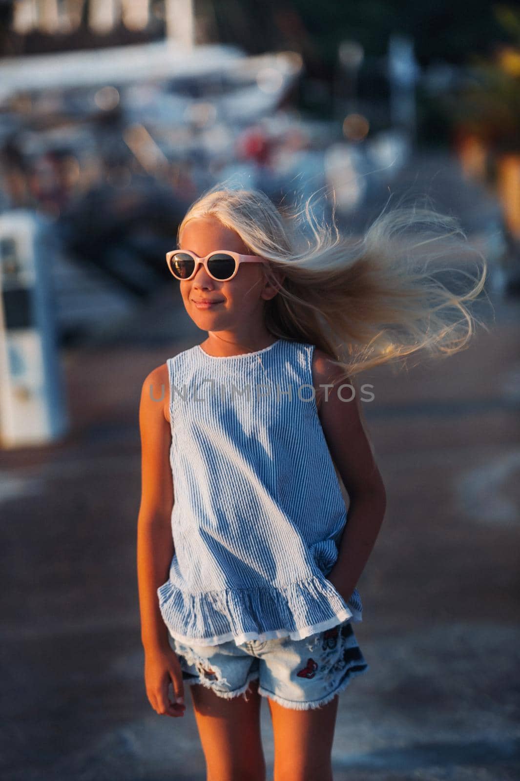 Portrait of a cute smiling ten-year-old girl with glasses.A girl in shorts and a blue t-shirt at sunset near the sea.Turkey