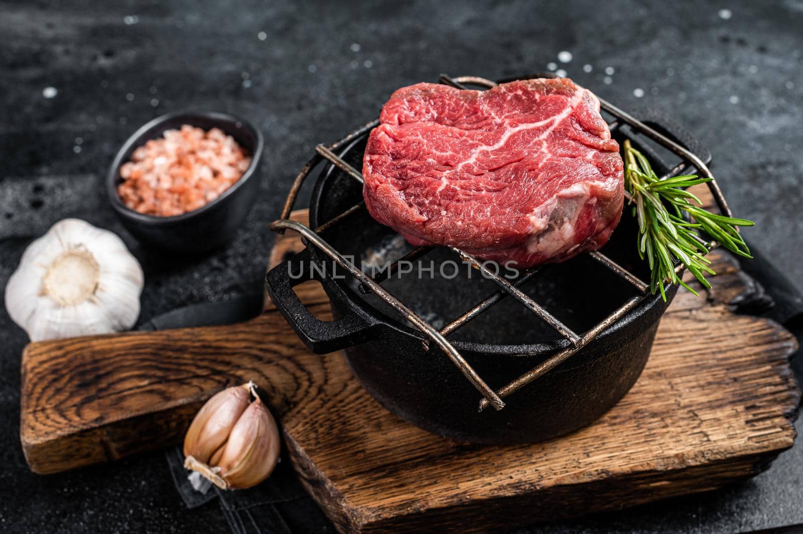 Raw fillet mignon beef steak on a grill with herbs. Black background. Top view.