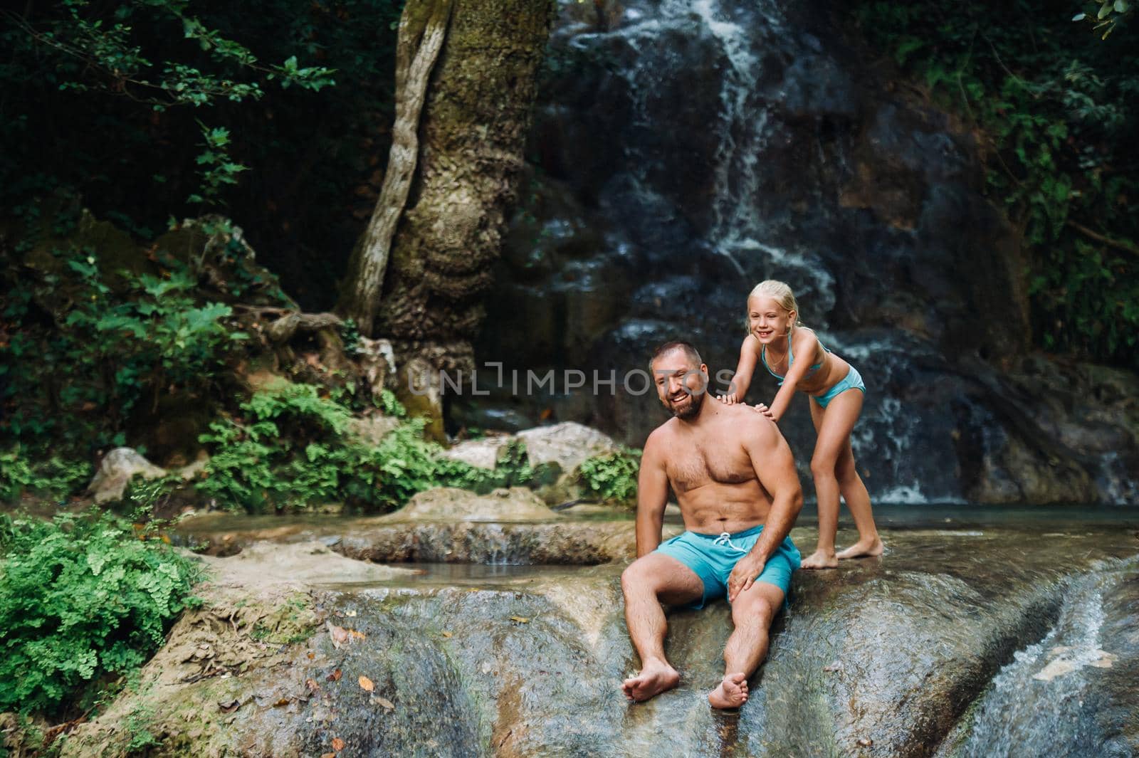 Father with daughter near a waterfall. Traveling nature near a beautiful waterfall, Man and a little girl stand and enjoy the view of the waterfall. by Lobachad