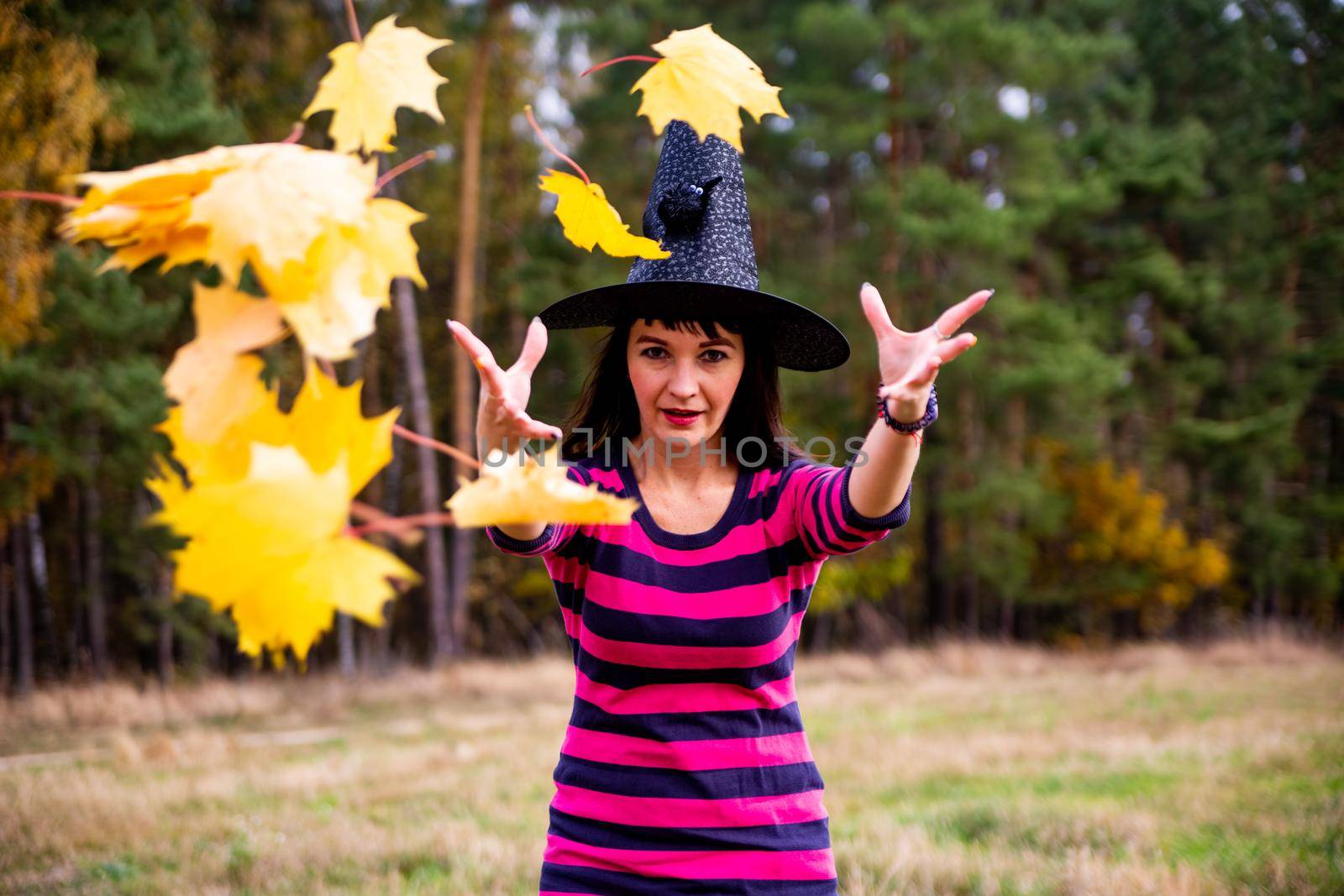 witch throws leaves in the autumn forest. Halloween costume party magician woman