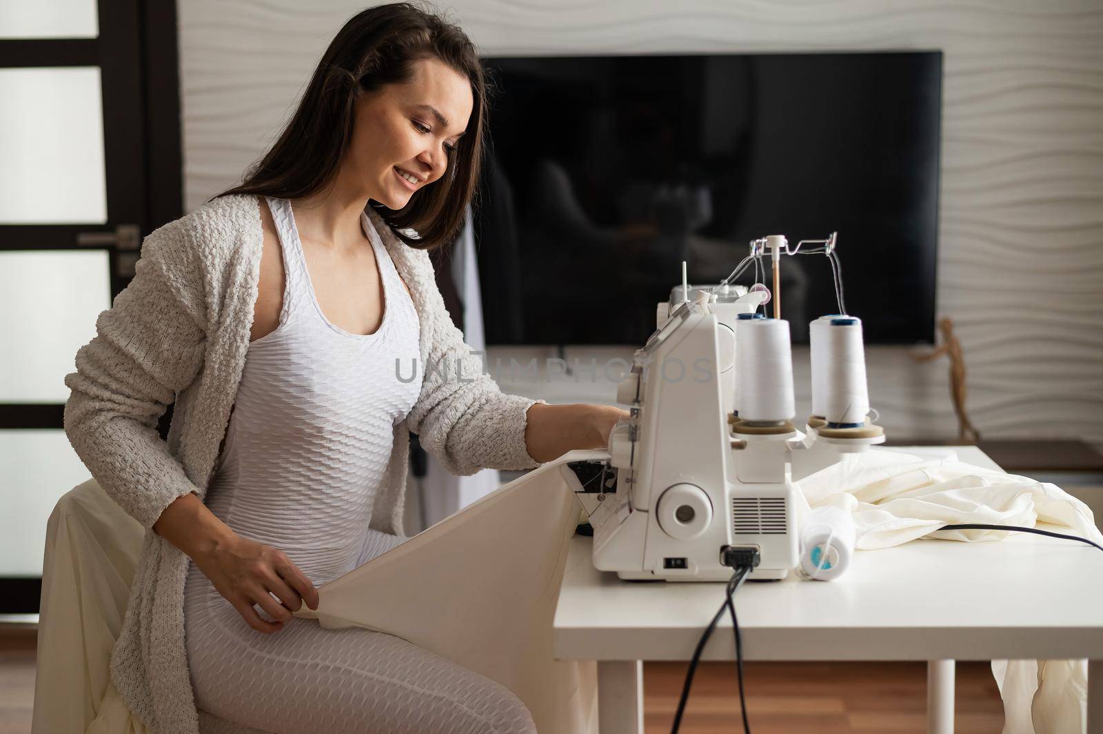 Caucasian woman sews to order at home. Work space of a seamstress in the living room.