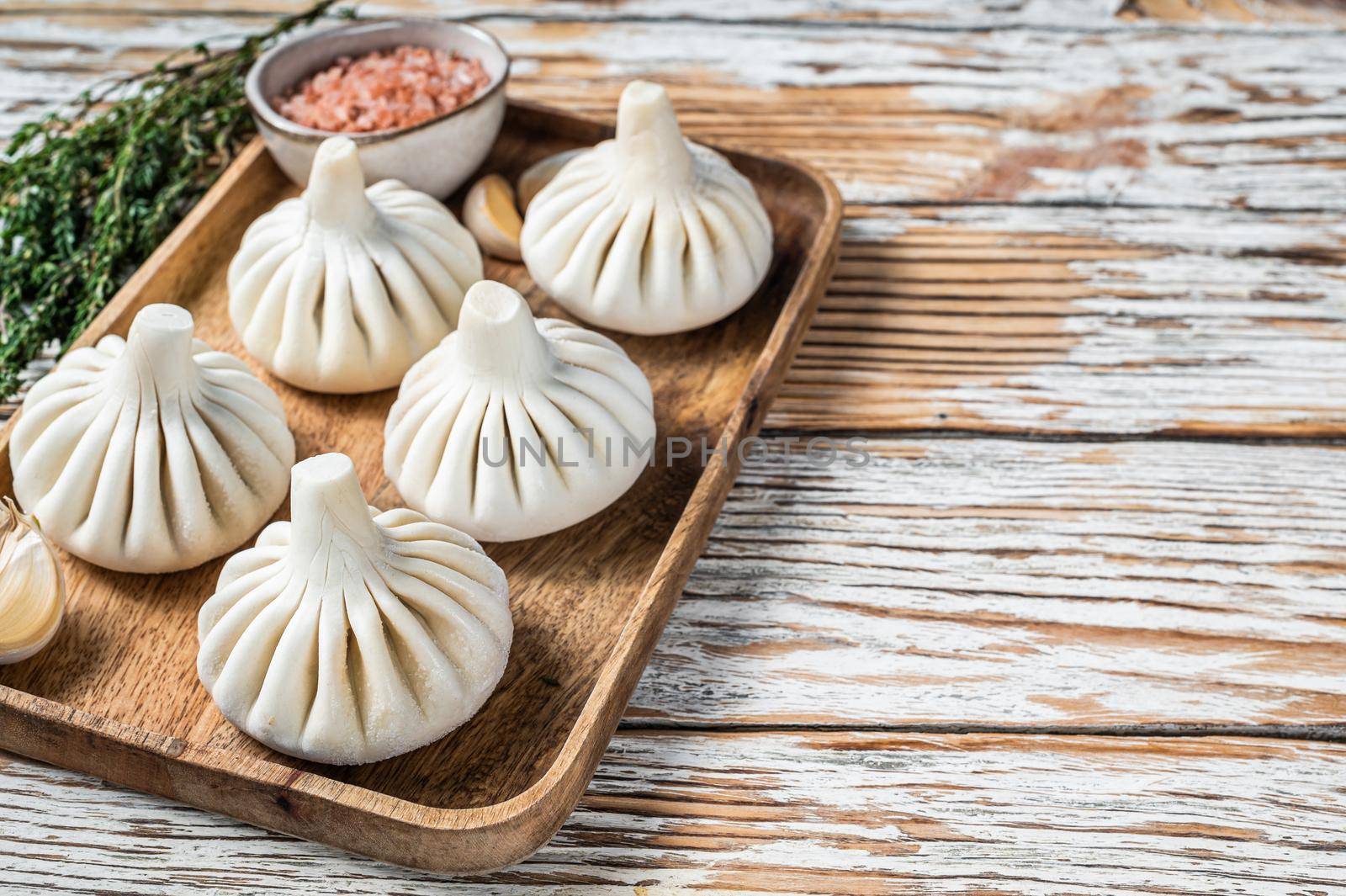 Frozen Raw dumplings Khinkali with beef and lamb meat on wooden tray with herbs. White wooden background. Top view. Copy space.