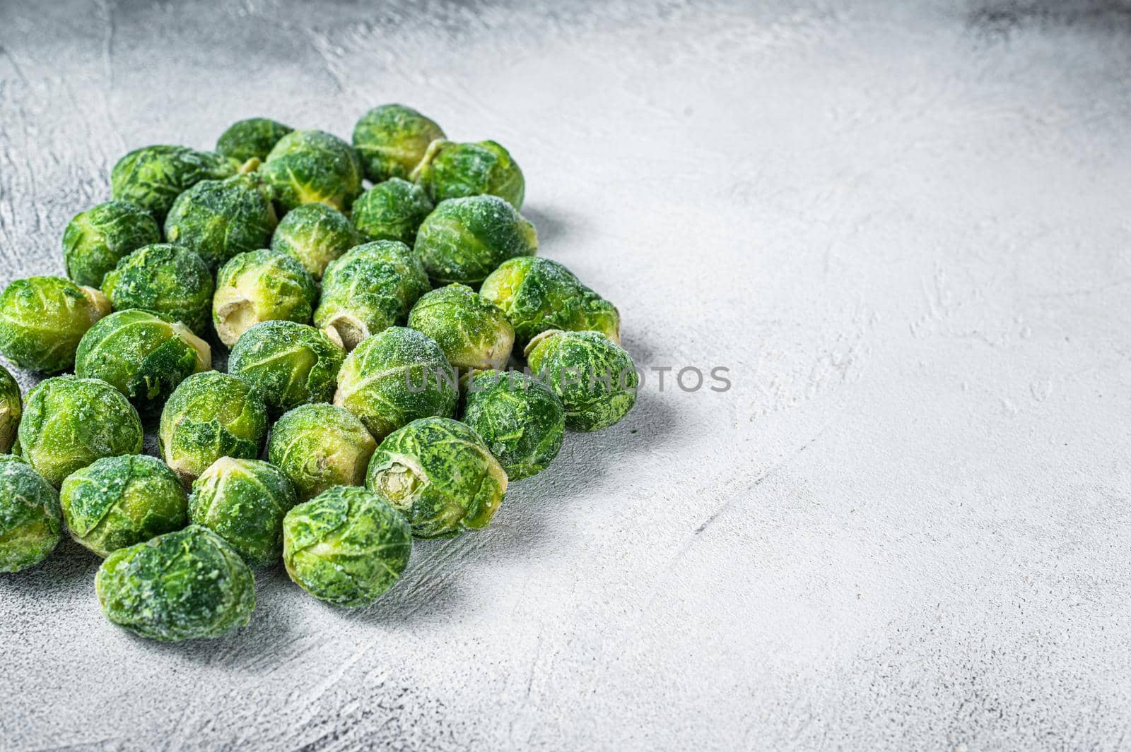 Frozen Brussels sprouts green cabbage on kitchen table. White background. Top view. Copy space by Composter