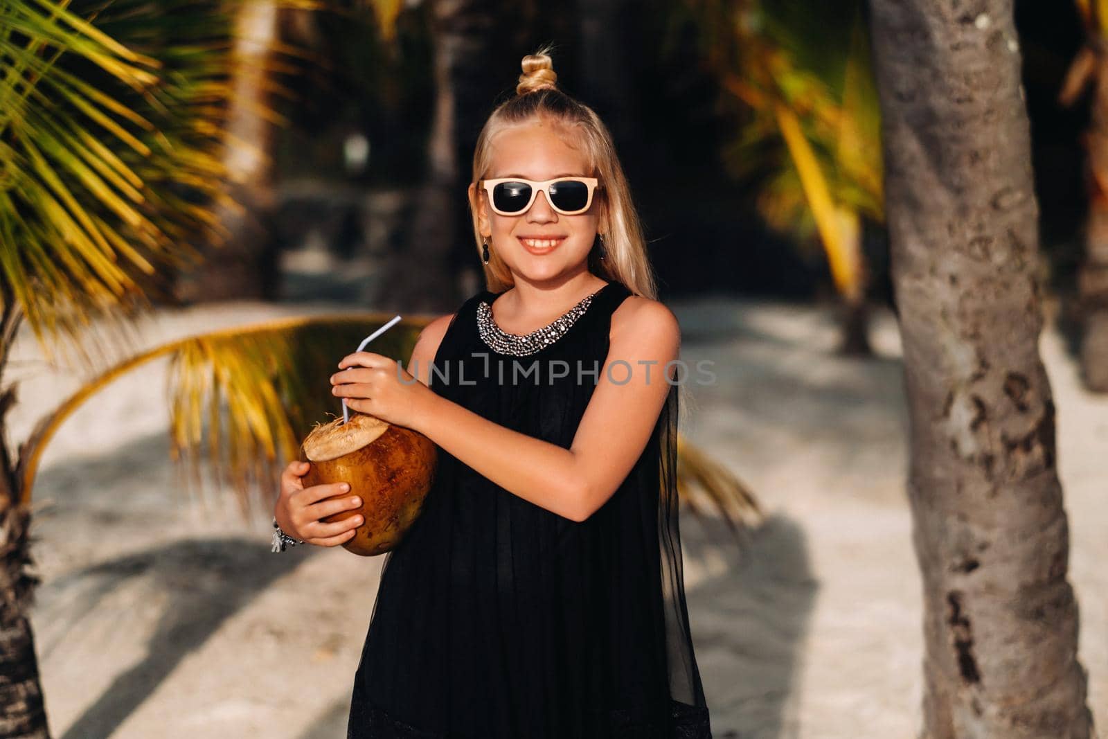Portrait of a cheerful 9-year-old girl with a coconut cocktail on the background of palm trees on an exotic beach.little Girl with a coconut on the beach of the island of Mauritius.