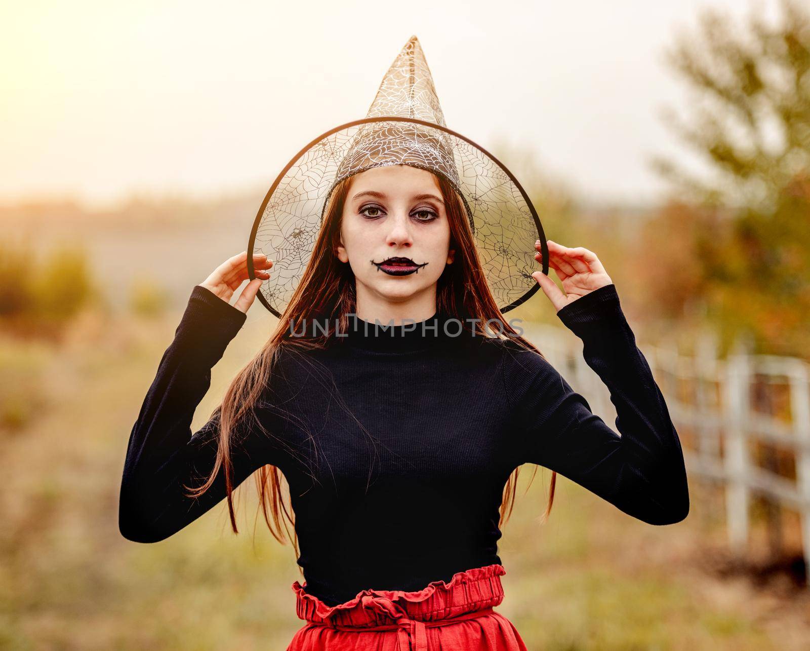 halloween portrait of teenage girl in witch hat smiling at camera on nature background