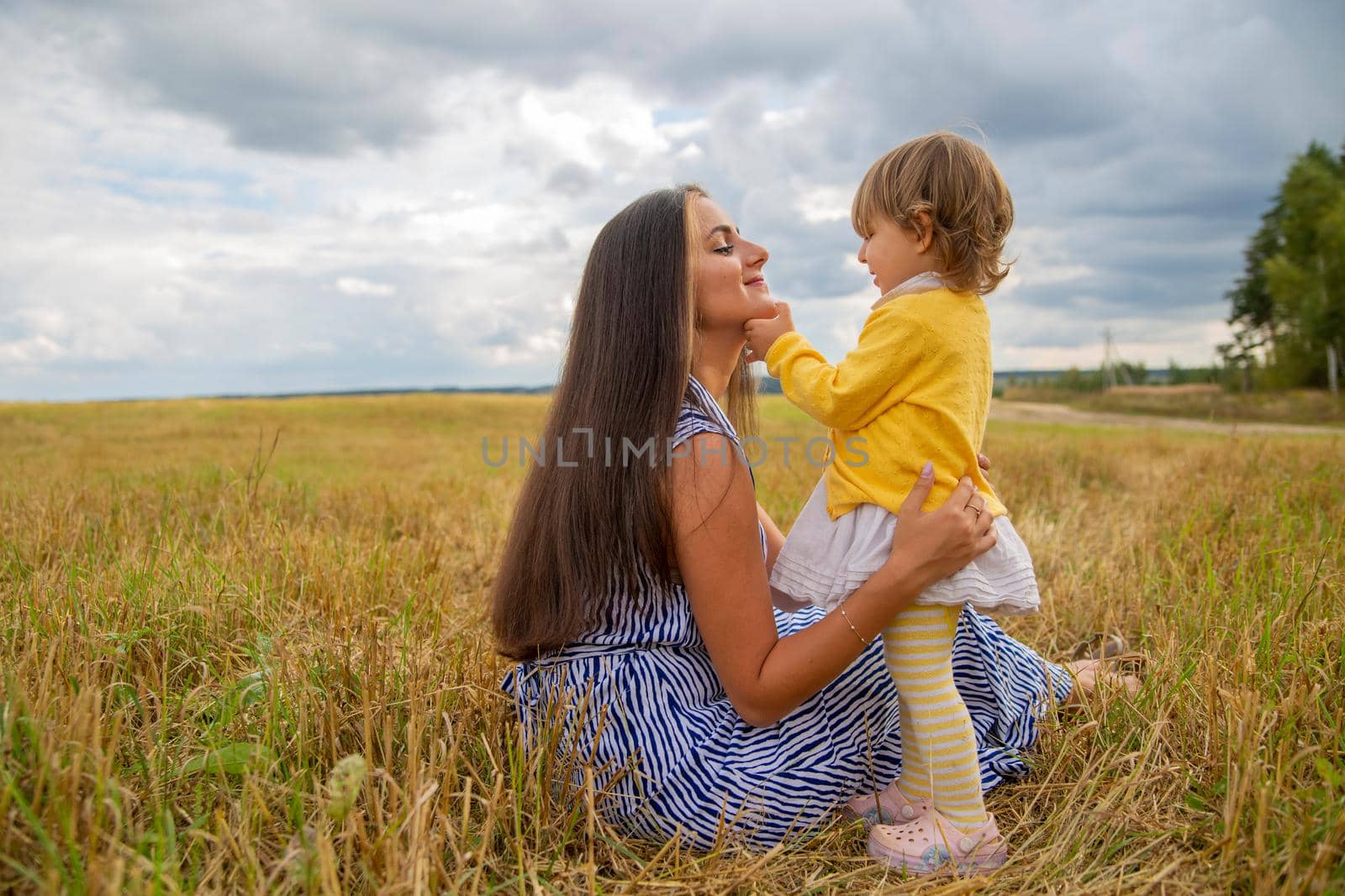 Happy family in the field of blew flowers. Beautiful young mother hugs her adorable baby girl. Concept of happiness by Mariaprovector