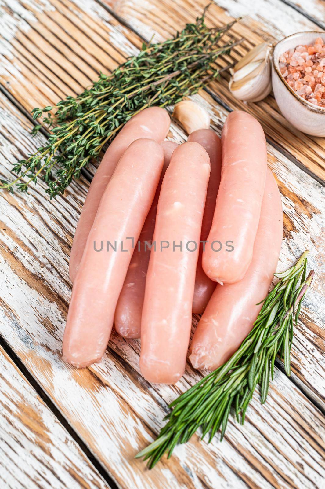 Raw Chicken sausages on a wooden kitchen table with herbs. White wooden background. Top view by Composter