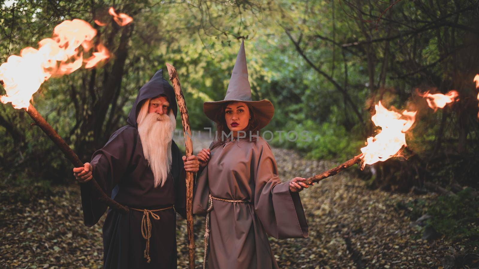 Wizard and sorceress in the autumn forest. Elderly man and woman in carnival costumes for halloween.