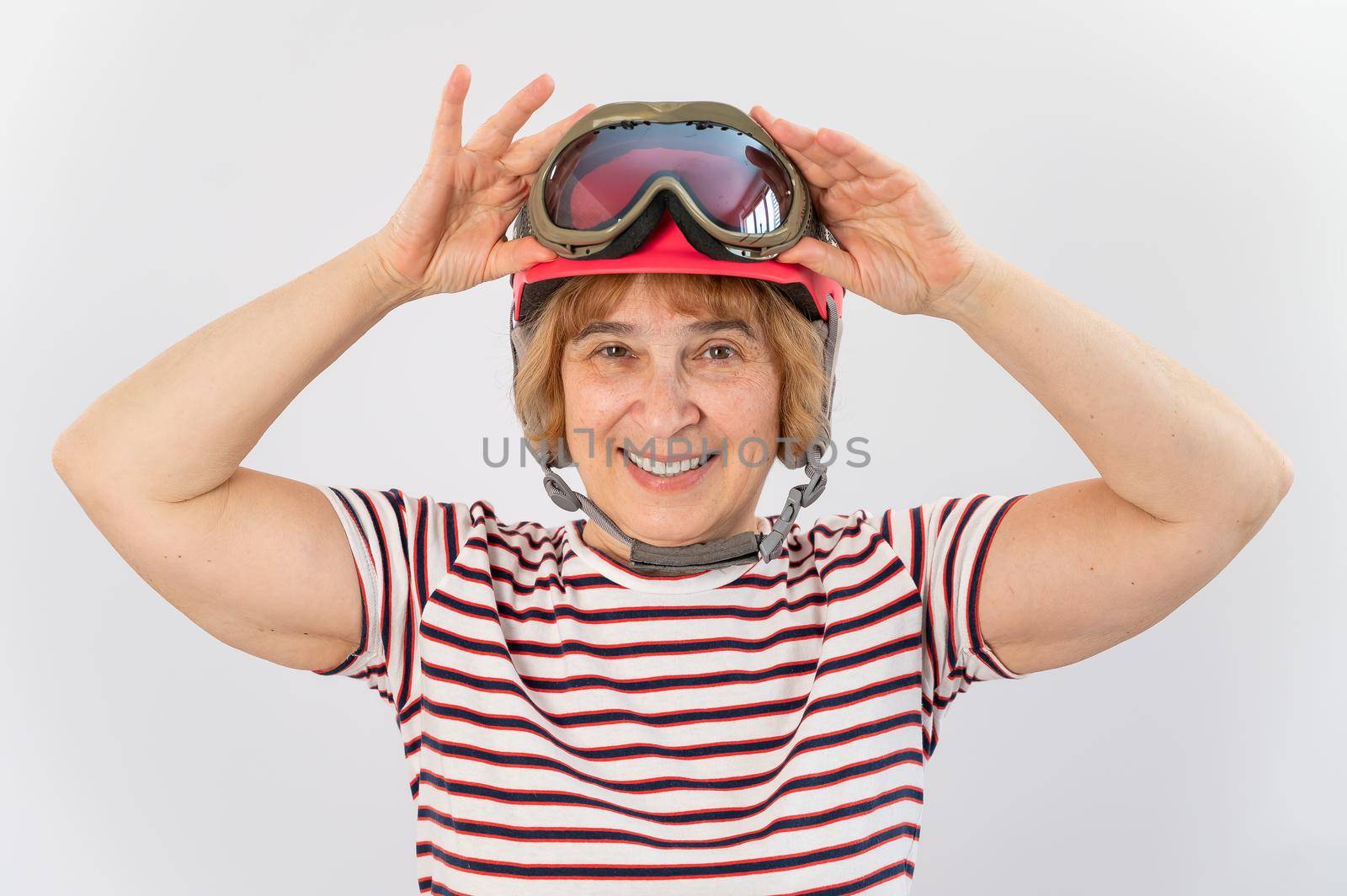 An elderly woman puts on a pink ski helmet on a white background by mrwed54