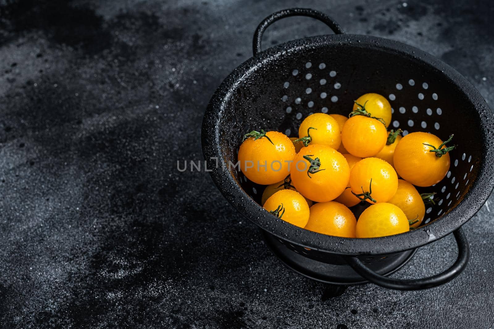Yellow cherry tomato in a colander. Black background. Top view. Copy space by Composter