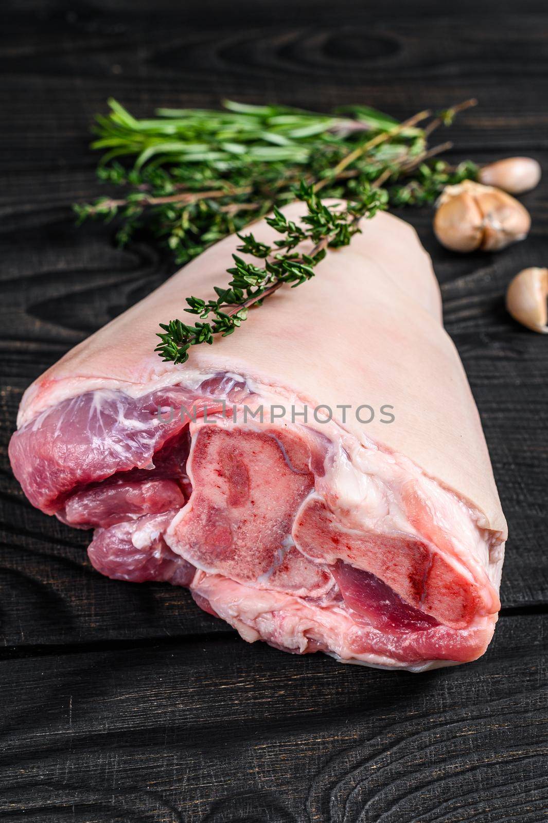 Raw Pork knuckle leg meat on kitchen table with herbs. Black wooden background. Top view.