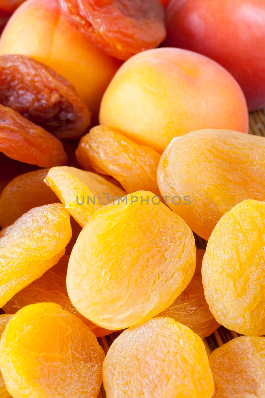 a pile of orange and yellow dried dried apricots, lying together with fresh and ripe apricots on a wooden table, close-up photo