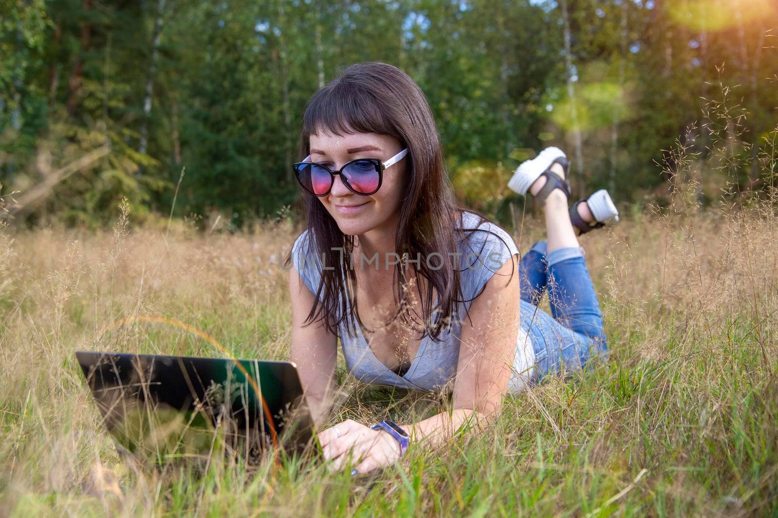 beautiful young woman emotionally working on a laptop on a sunny lawn on a warm summer day. happy remote freelancer