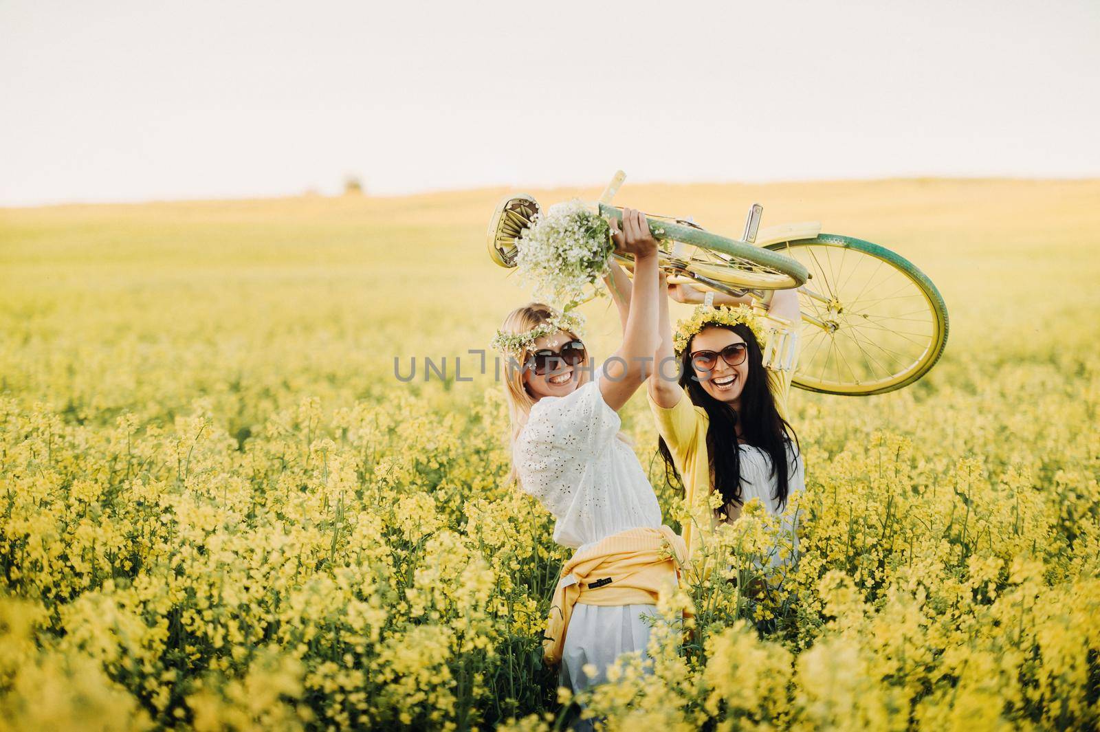 two women in a rapeseed field with a bicycle enjoy a walk in nature rejoicing.
