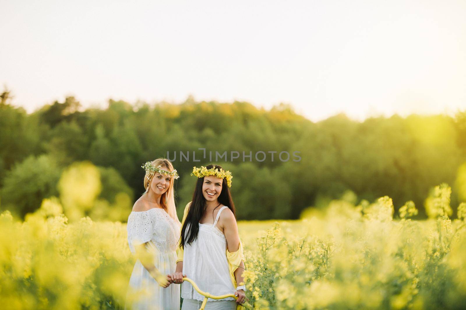 two women in a rapeseed field with a bicycle enjoy a walk in nature rejoicing by Lobachad
