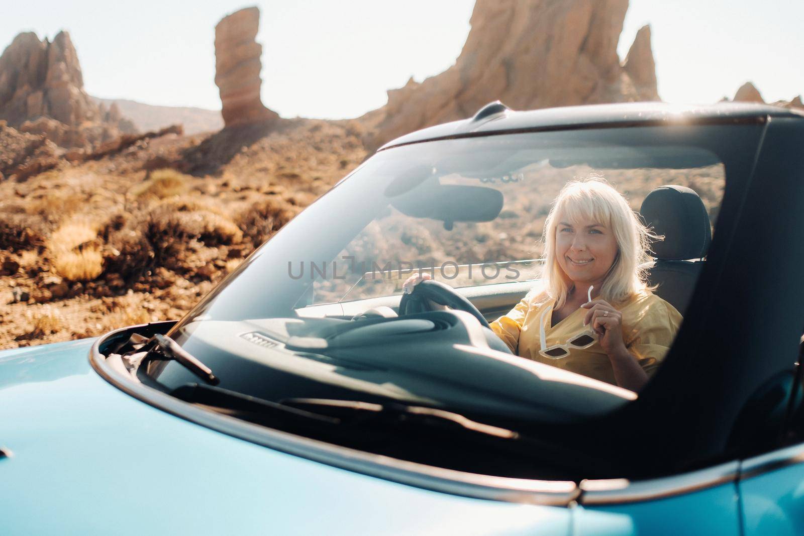 Girl in yellow dress enjoying a road trip in a convertible through a deserted valley with mountains, Canary Islands, Tenerife