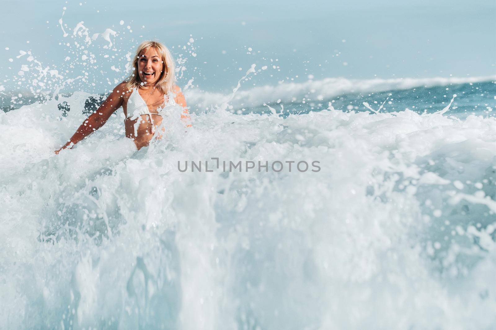 A girl with wet hair jumps over large waves in the Atlantic ocean, around a wave with splashes of spray and water drops.Tenerife.Spain by Lobachad