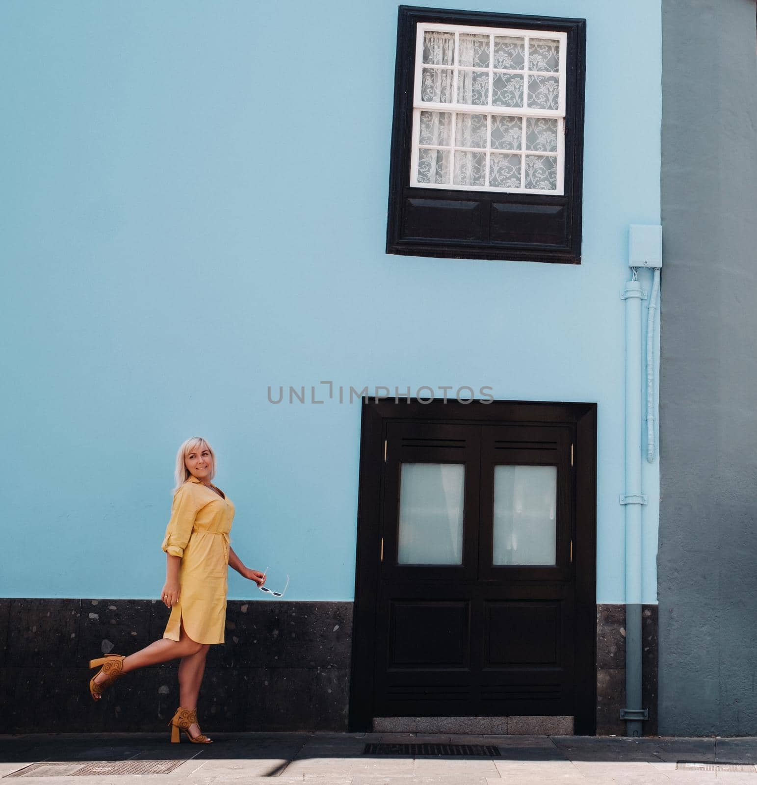 a blonde woman in a yellow summer dress stands on the street of the Old town of La Laguna on the island of Tenerife.Spain, Canary Islands by Lobachad