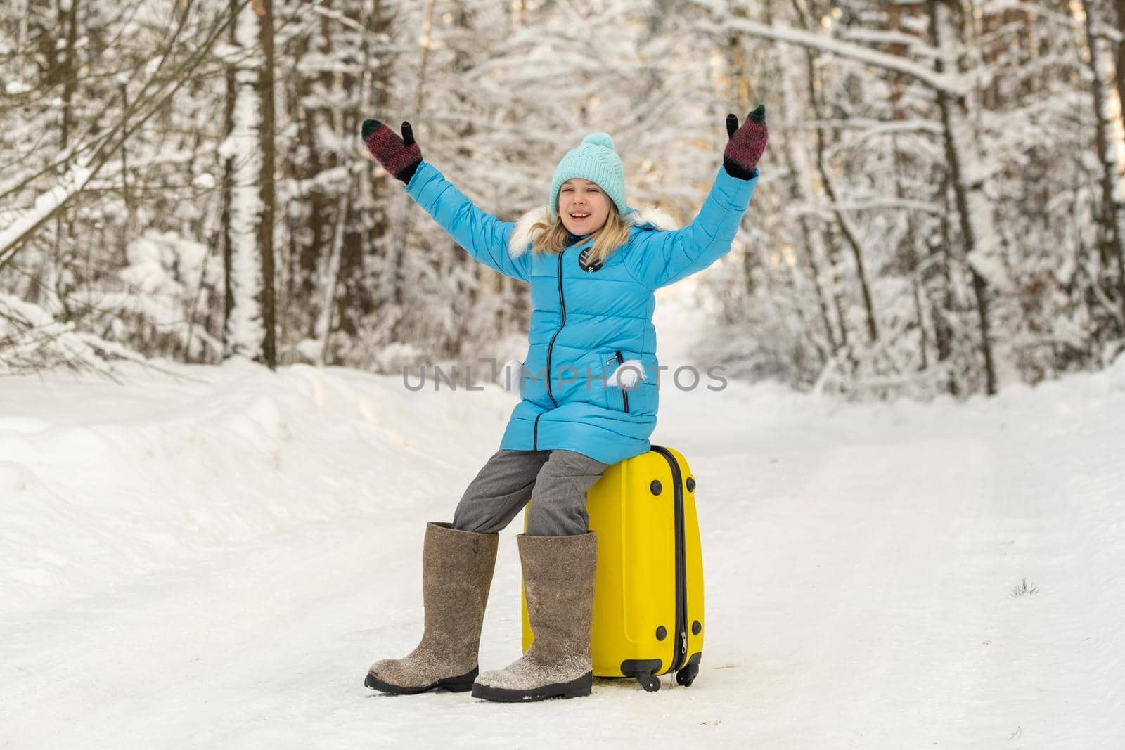 A girl in winter in felt boots sits on a suitcase on a frosty snowy day by Lobachad