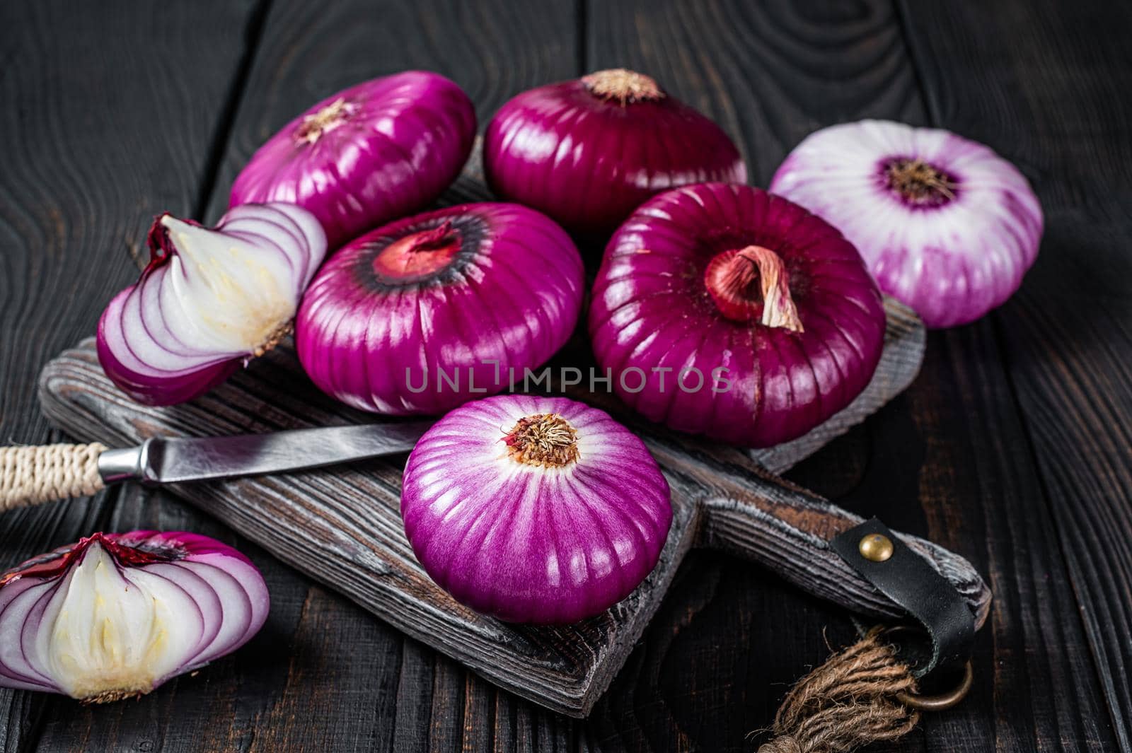 Whole and halfed Flat red sweet onion on a cutting board. Black Wooden background. Top View by Composter