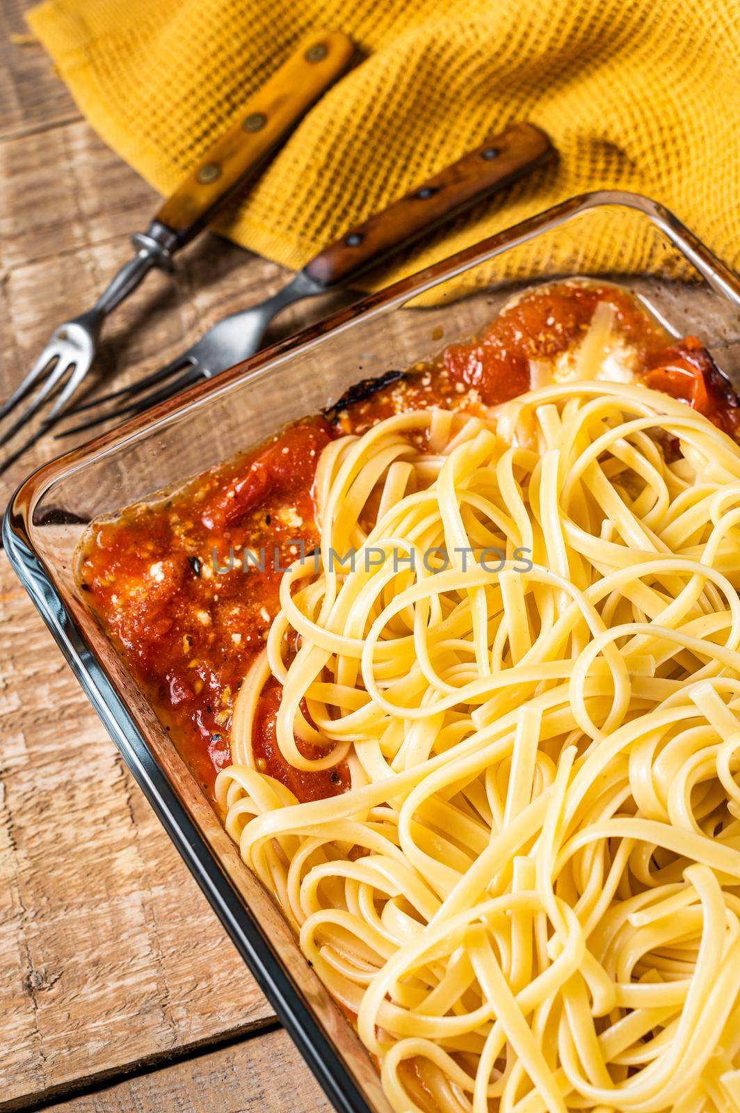 Oven roasted feta pasta with tomatoes in baking dish. Wooden background. Top view by Composter