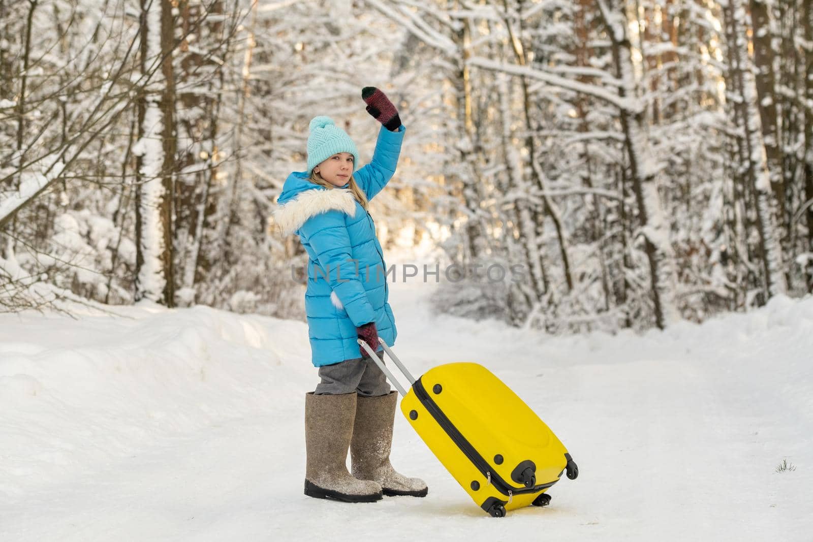 A girl in winter in felt boots goes with a suitcase on a frosty snowy day by Lobachad