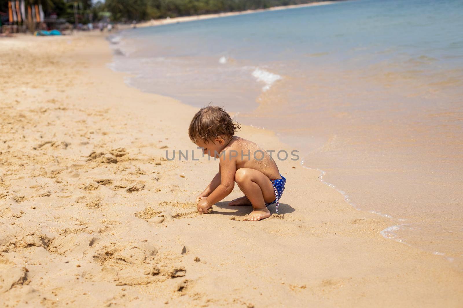adorable toddler toddler has fun playing on sandy beach of tropical sea.