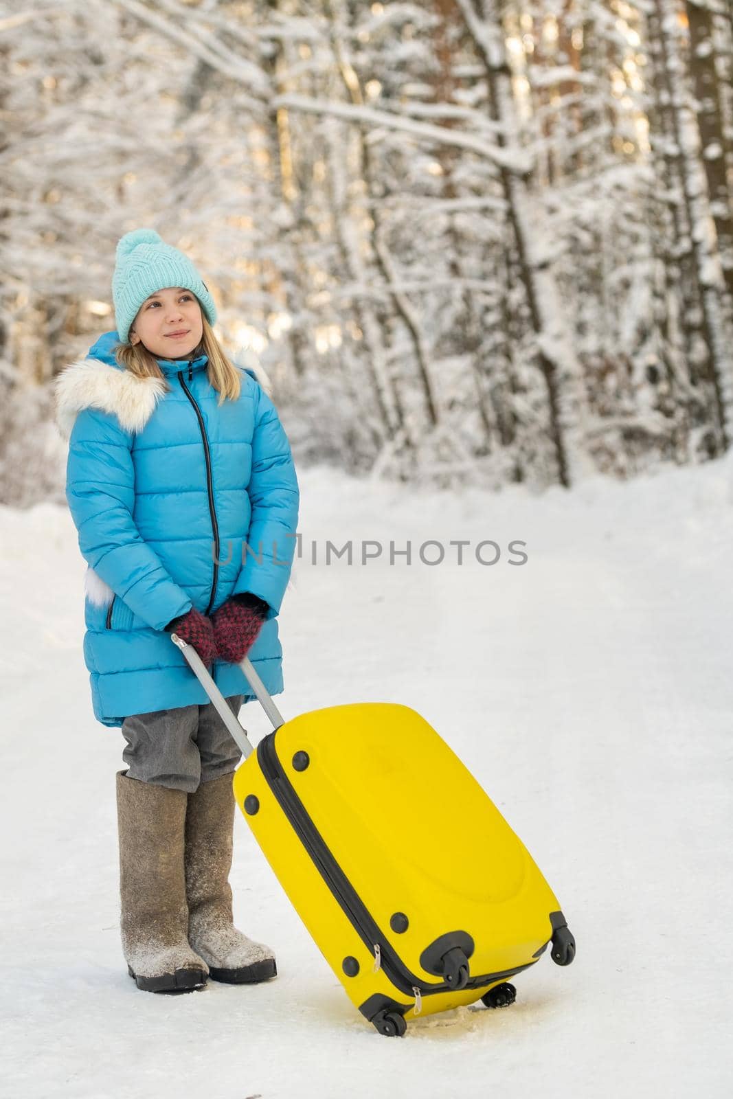 A girl in winter in felt boots goes with a suitcase on a frosty snowy day.