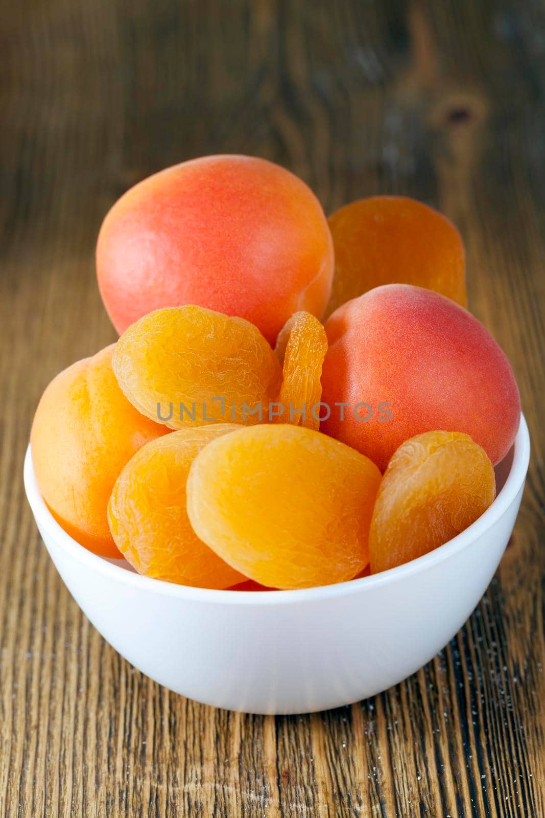 fresh and dried apricots lying in a white bowl on a wooden table, close-up photo