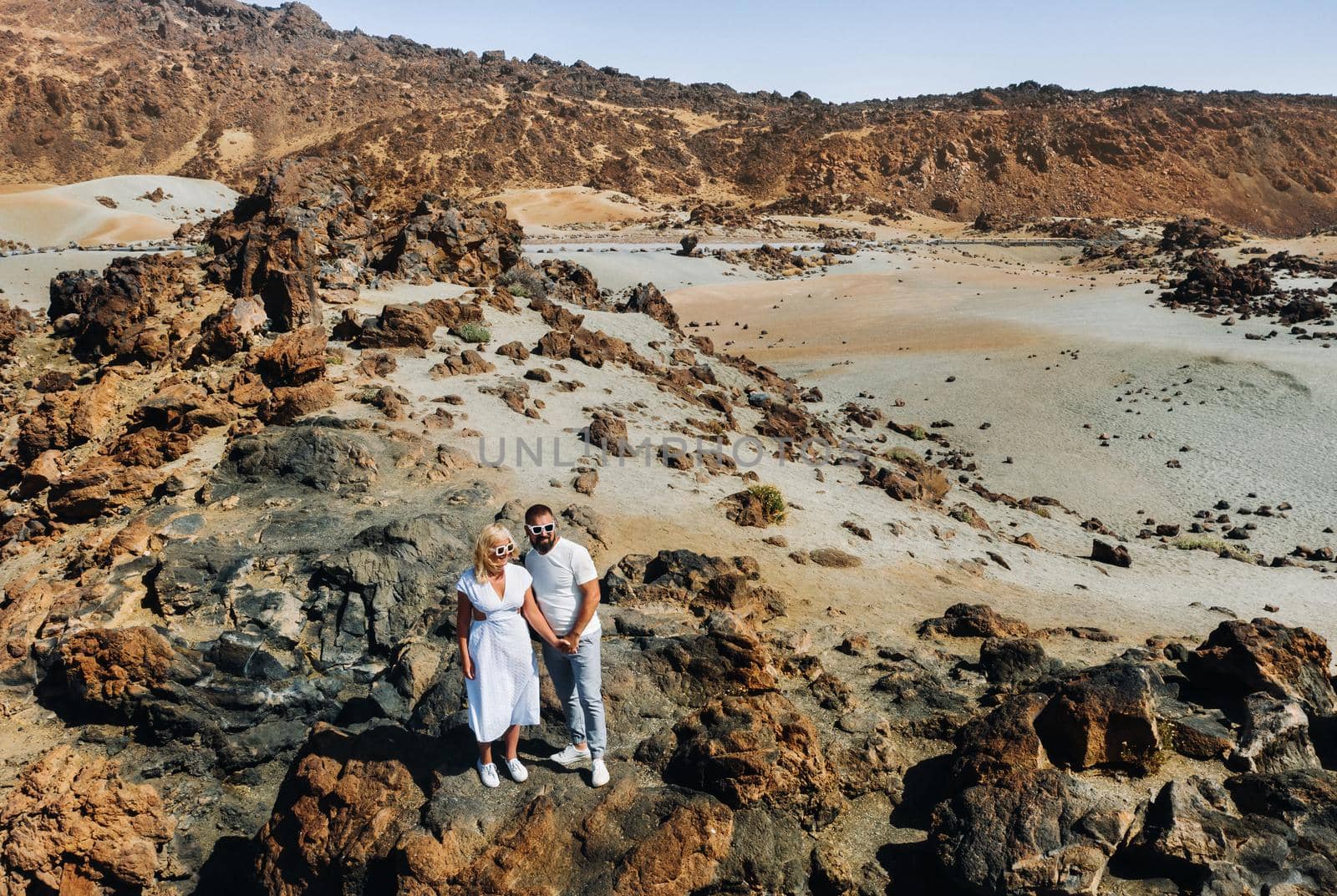 a guy and a girl in white clothes and glasses stand in the crater of the El Teide volcano, a Couple stands on a mountain in the crater of a volcano on the island of Tenerife, Spain.