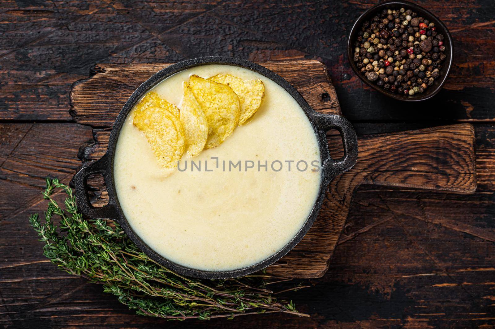 Potato cream soup with potato chips in pan on wooden board. Dark wooden background. Top view by Composter