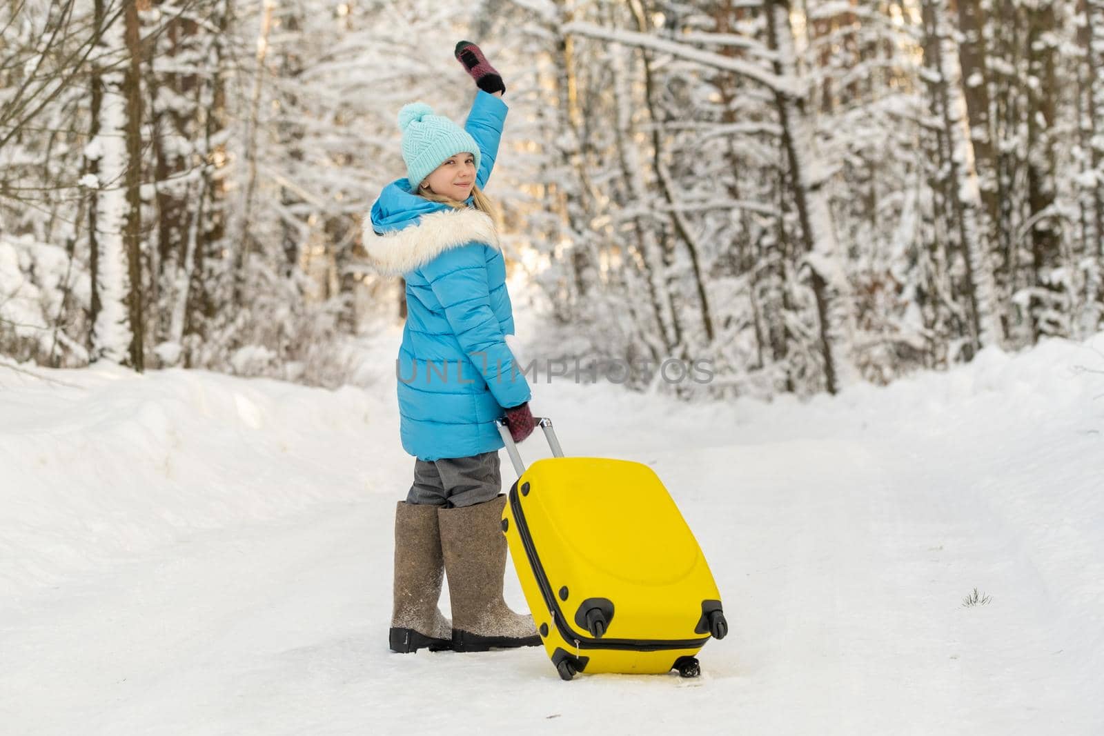 A girl in winter in felt boots goes with a suitcase on a frosty snowy day.