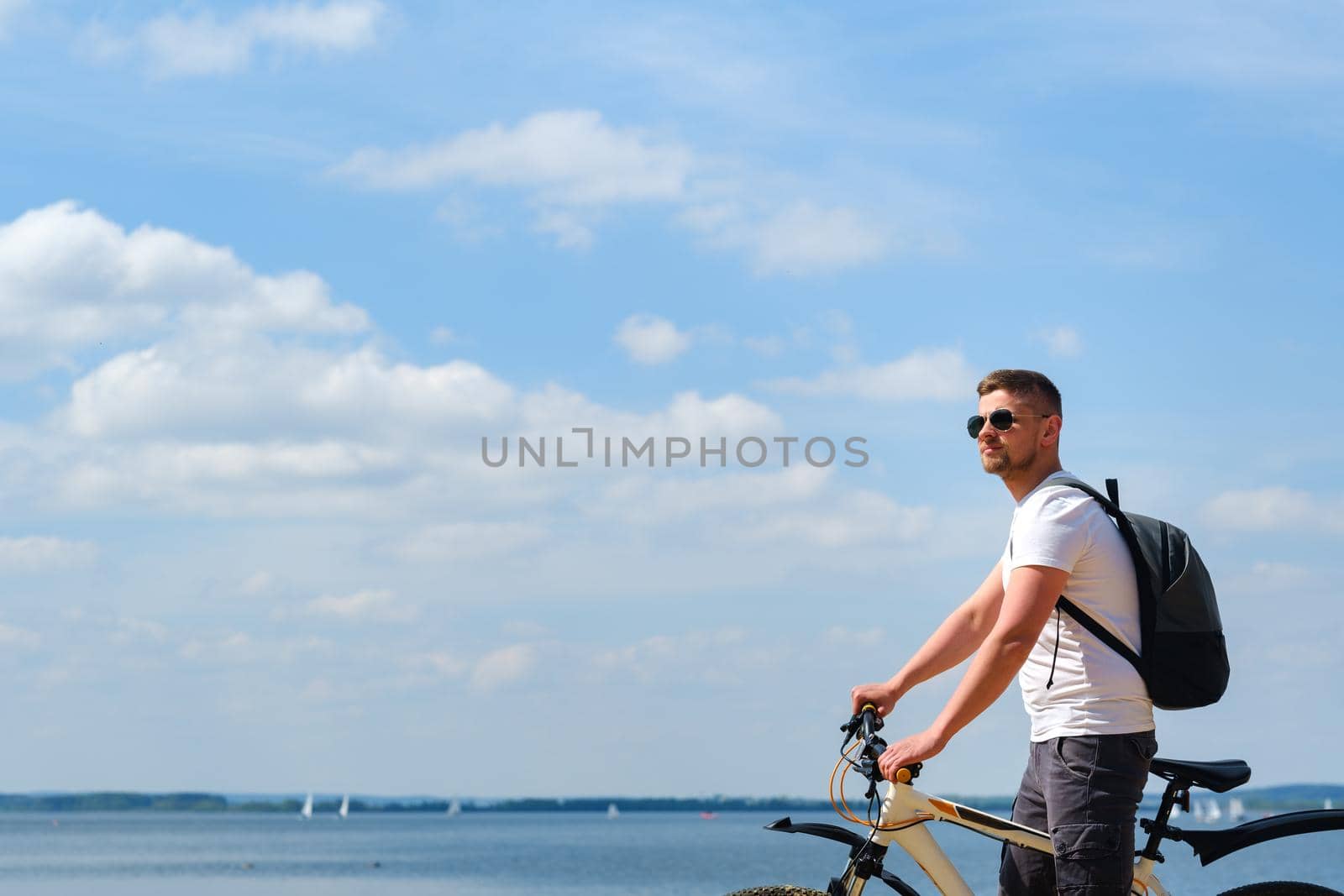 A cyclist with a backpack and glasses rides along the sea on a bicycle on a beautiful sunny day.