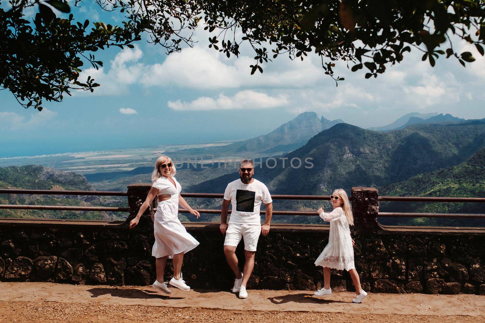 a happy family, a man, a woman and a daughter, are jumping merrily against the background of mountains and jungles of the island of Mauritius.A couple and daughter in the jungle of the island of Mauritius in white clothes walking in Africa, by Lobachad